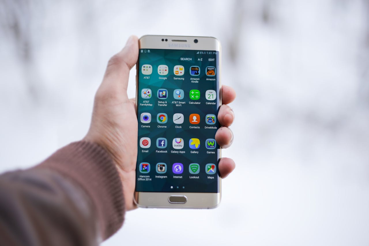Hand holding a Samsung smartphone displaying colorful app icons on screen